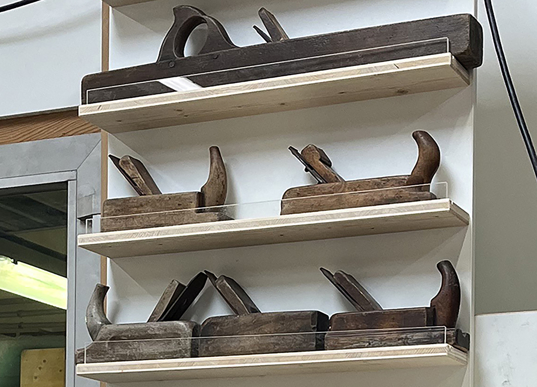 Wandpanel mit historischen Hobeln auf Regalböden.