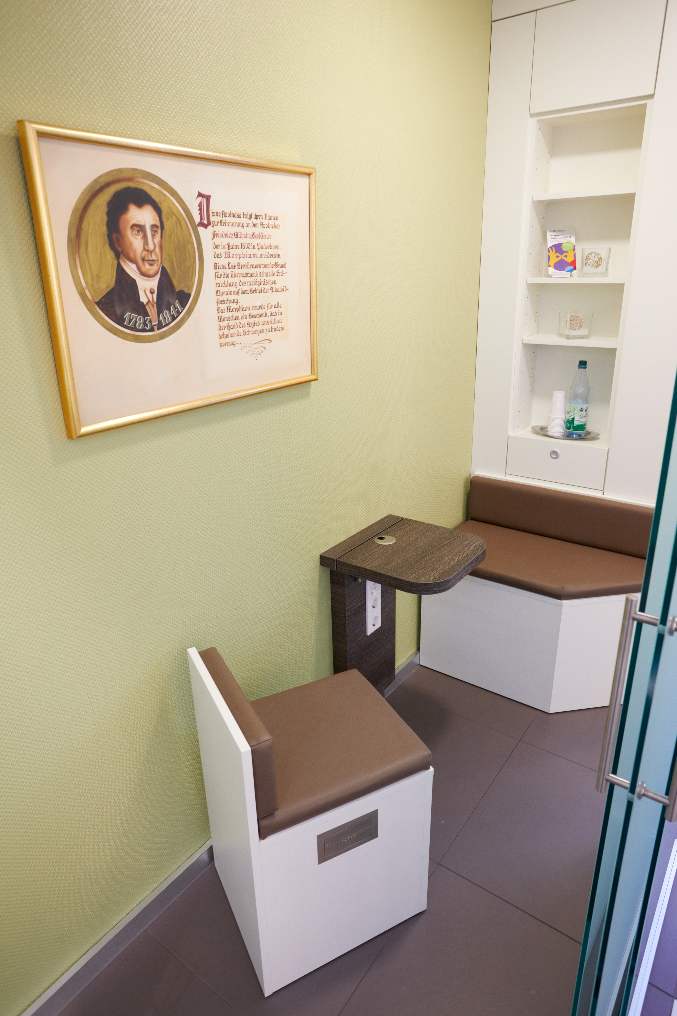 Ein Zimmer mit Sitzgelegenheiten, kleinem Tisch und einem Bild mit Zitat an der Wand.