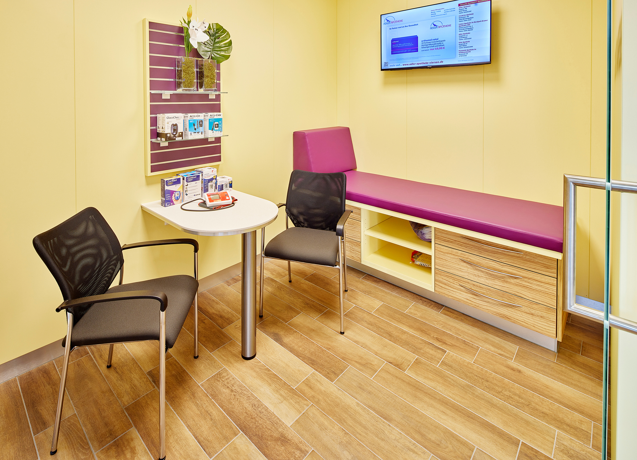 Ein kleiner Behandlungsraum mit Tisch, Stühlen und Liegematte.