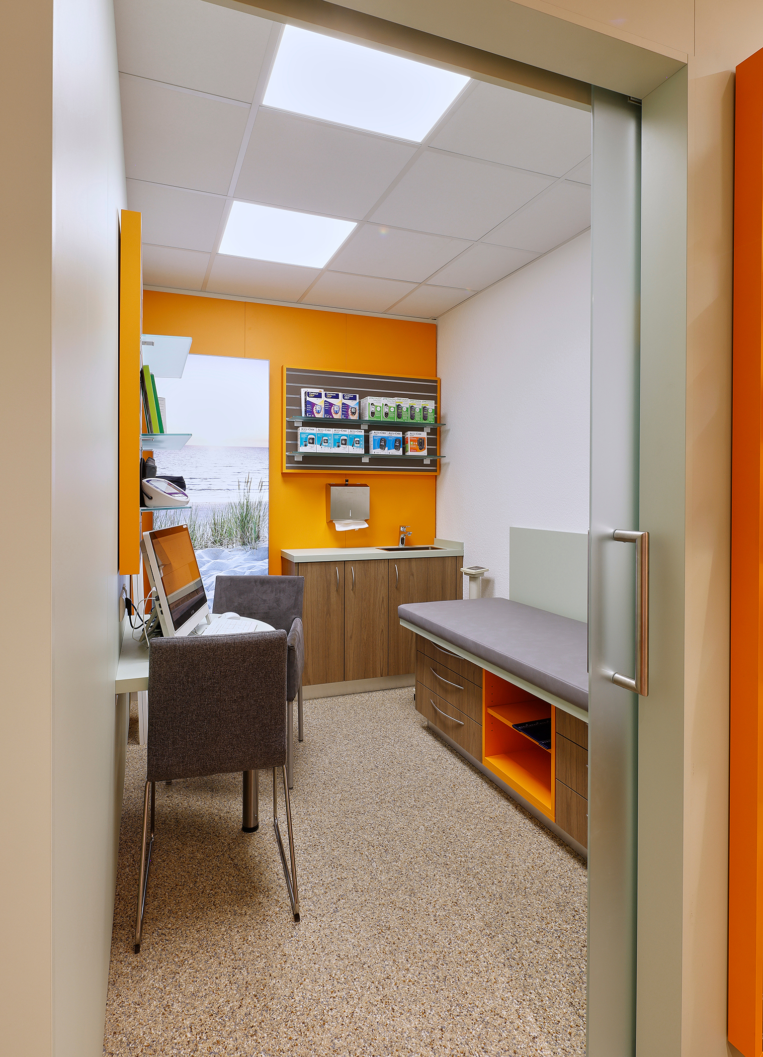 Ein kleiner Behandlungsraum mit Tisch, Stühlen, Liegematte und Computer.