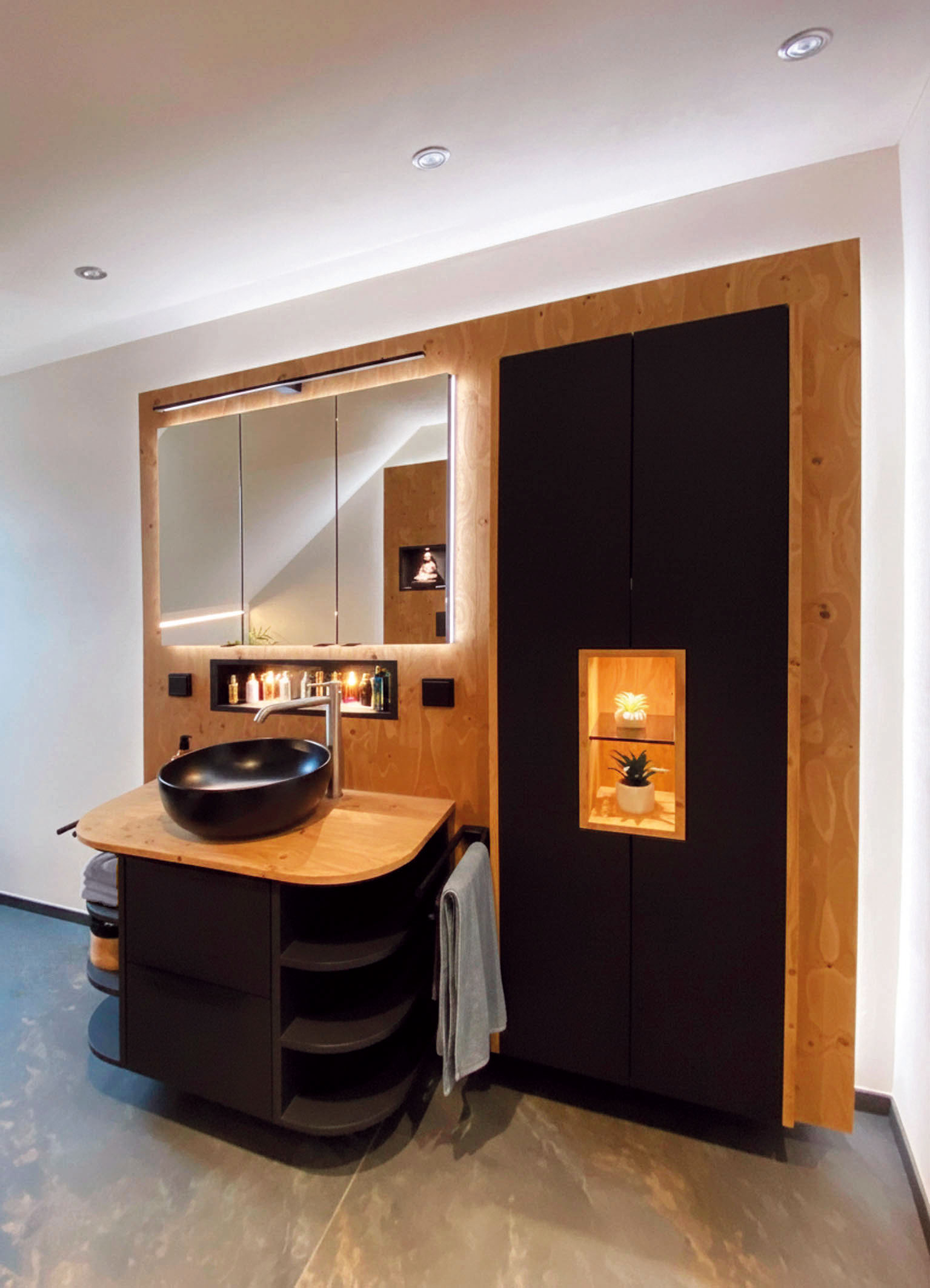 Badmöbel hinterleuchtete Wand in Holz mit schwarzem Unterschrank und schwarzem Hochschrank mit beleuchteten Fächern.