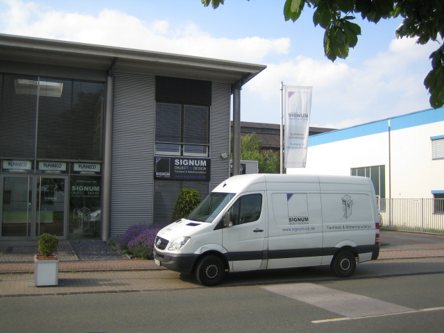 Ein weißer Firmenwagen mit SIGNUM Logo vor dem Firmengebäude geparkt.