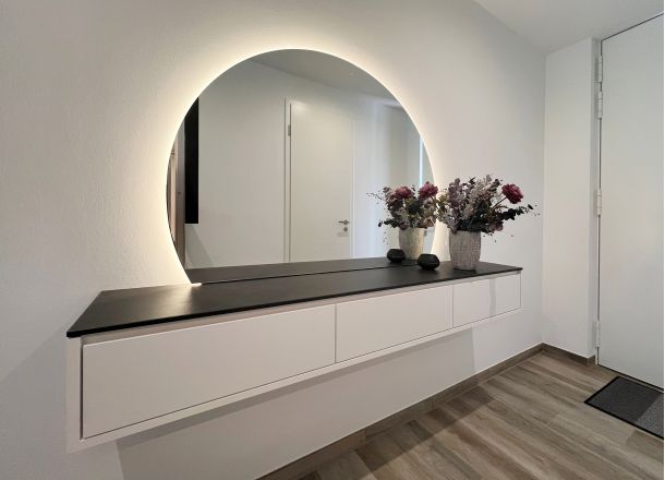Sideboard mit Schubladen in Eingangsbereich mit halbrundem, beleuchtetem Spiegel.