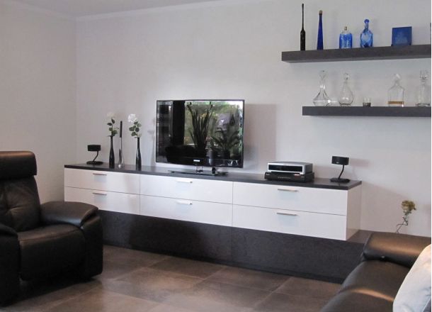 Wohnzimmer mit TV-Möbel in Weiß-Schwarz, Dekovasen, Technikgeräten und schwebenden Regalen mit Glasflaschen.