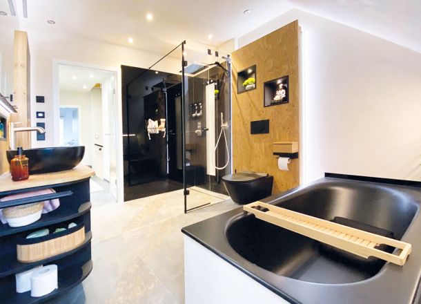 Ein Badezimmer mit WC, Dusche, Wanne und Waschbecken in schwarz und Einrichtung in schwarz mit Holz kombiniert.