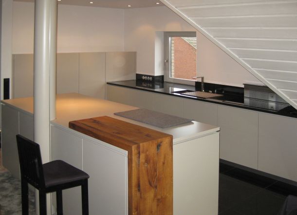 Eine dezente Küche in Lichtgrau mit Kochinsel und angesetztem Tischelement in Massivholz.