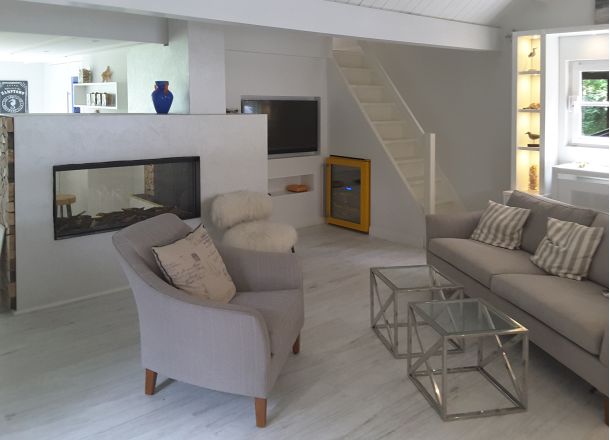 Ein modernes Wohnzimmer mit Couch, Sessel, TV und Kamin und eingelassenem Weinkühlschrank in Verkleidung unter Treppe.