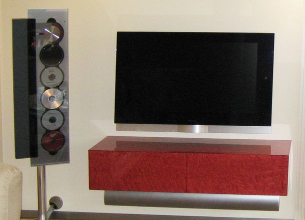 Ein Wand-Fernseher mit schwebender Kommode in weinrot gebeiztem Vogelaugenahorn hochglänzend lackiert, einer Soundbar darunter und B&O Anlage daneben.