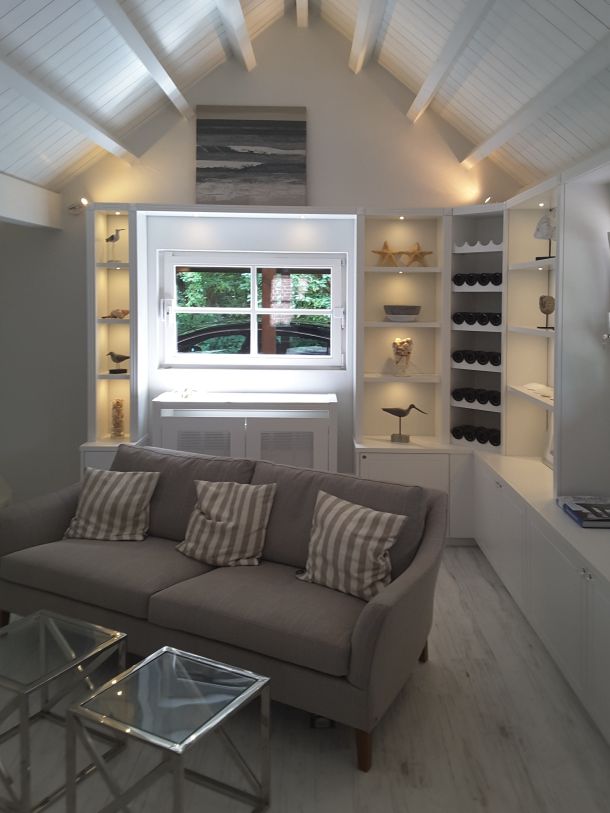 Ein modernes, skandinavisch wirkendes Wohnzimmer mit Couch , Einbauvitrinen mit maritimer Deko und Sprossenfenster.
