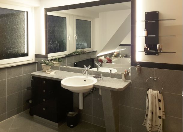 Ein Badezimmer mit in die Wand integriertem Waschbecken und großem Spiegel.