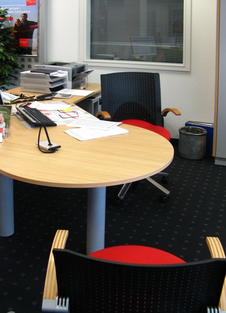 Ein Beratungsraum mit zwei Sesseln, einen dynamischen Schreibtisch auf dem Akten und Büroutensilien liegen.