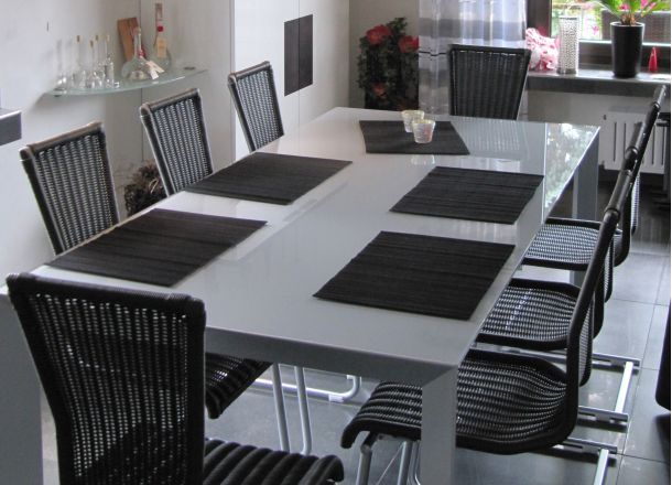 Moderner Essbereich mit weißem Hochglanztisch, acht schwarzen Geflechtstühlen und schwarzen Platzsets.