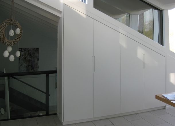 Einbauwandschrank mit weißer Schräge unter dem Dachfenster, nahtlos in die Architektur integriert, neben Treppenaufgang.