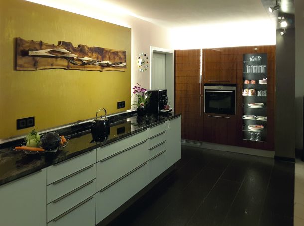 Eine moderne weiße Küche mit Gerätewand in hochglanzlackiertem Kirschbaum mit Weinkühlschrank und Holzbohlenbild über der Küchenzeile.