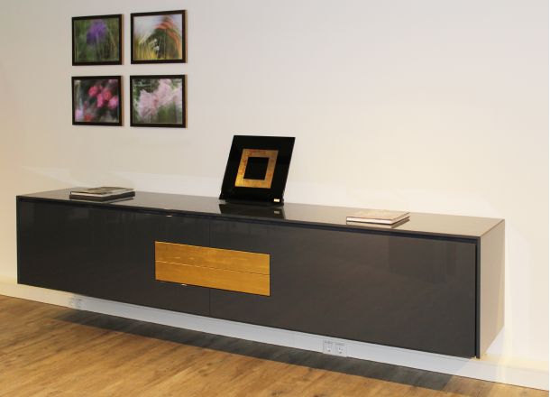 Schwebendes Sideboard in Schwarz mit Holzelement, Dekobild und Büchern, davor Holzboden, darüber vier gerahmte Fotos.