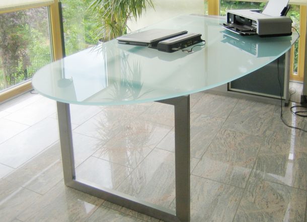 Ein Schreibtisch aus Glas mit einem Laptop und Drucker darauf.