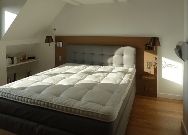 Ein Bett mit einem weißer Matratze und Kopfteil in Lack mit integrierter Beleuchtung und mit Ablagen.