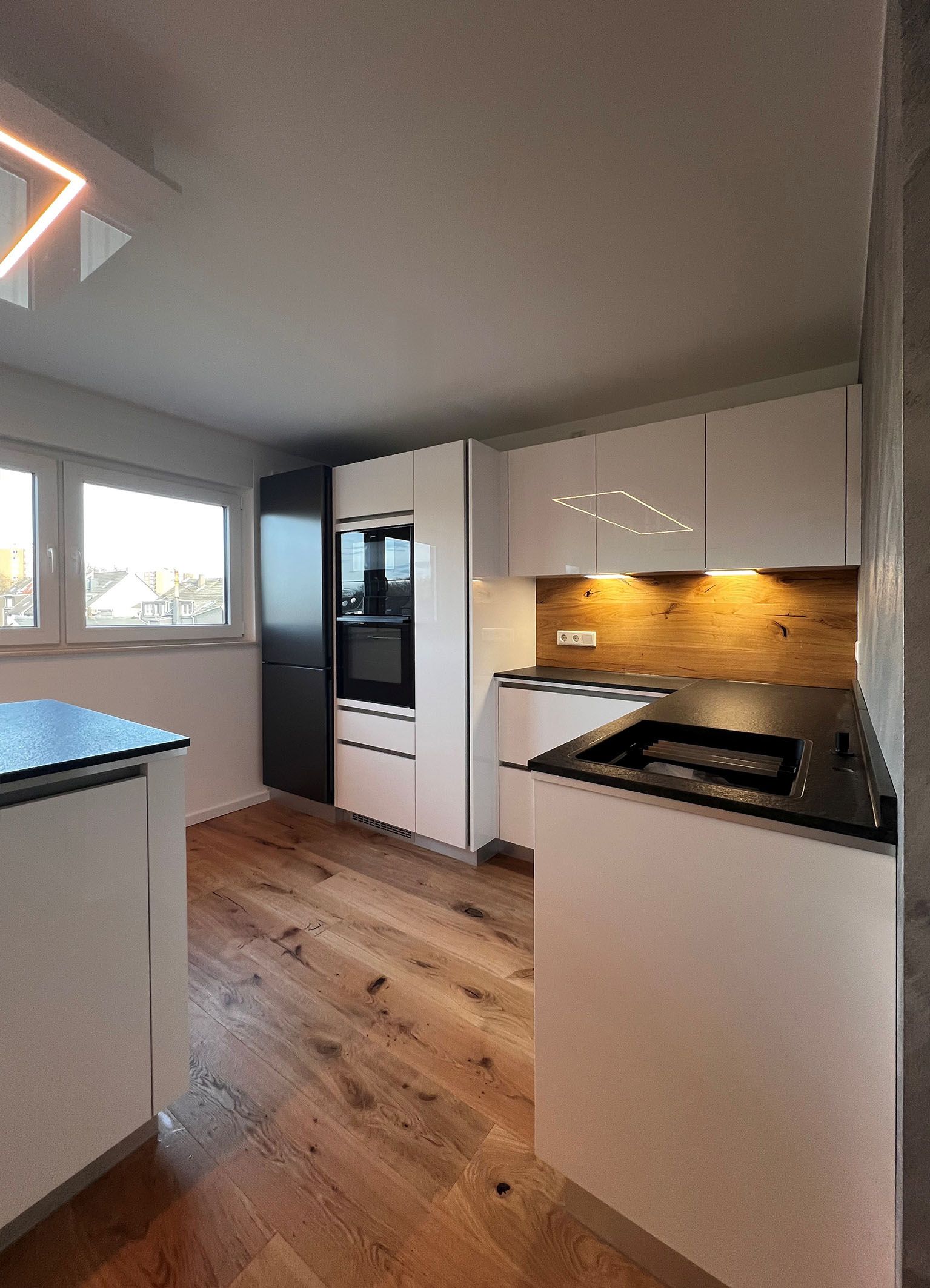 Küche mit weißen, grifflosen Fronten und Kühlschrank in schwarz.