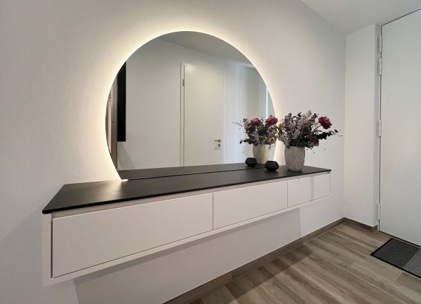 Sideboard mit 3 Schubkästen, Steindeckblatt und hinterleuchtetem Spiegel in Eingangsbereich.