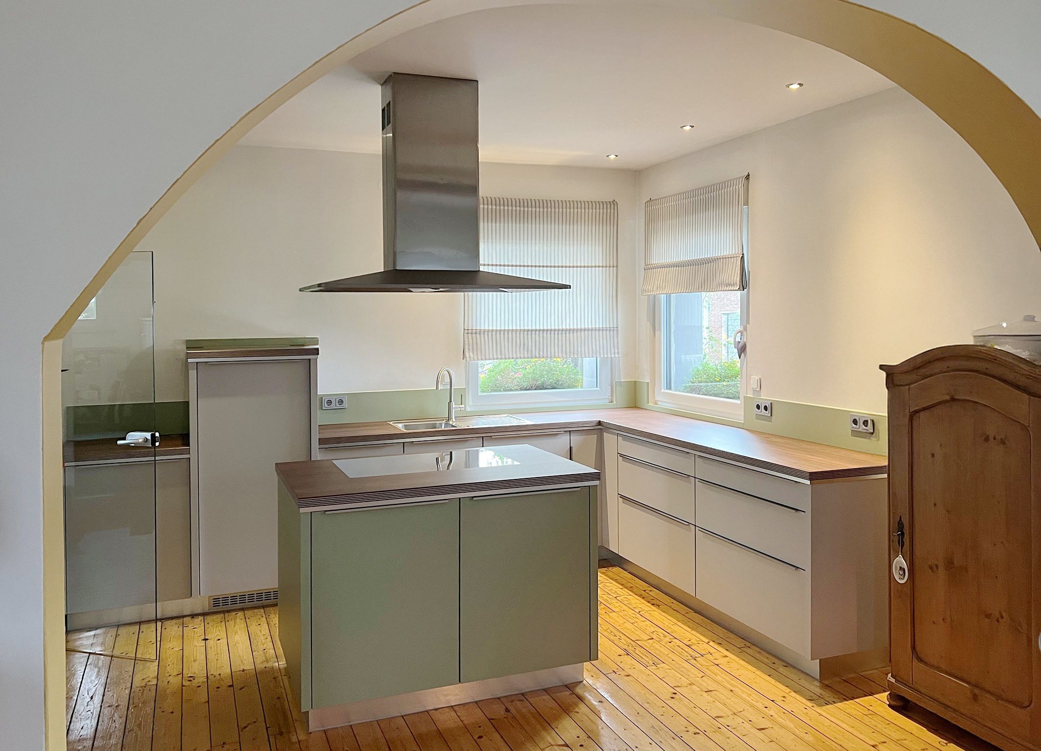 Helle Küchenmöbel mit Arbeitsplatten in warmem Holzton kombiniert mit sanftem Grünton, der sich auch in den Glasrückspiegeln wieder findet.