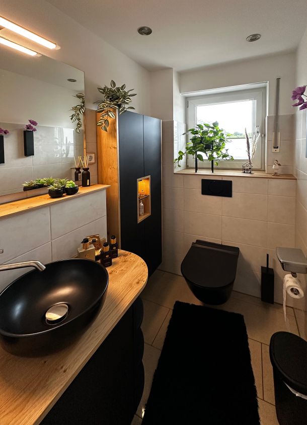 Badezimmer mit Keramik und Möbeln in schwarz mit Massivholz in Naturton kombiniert.